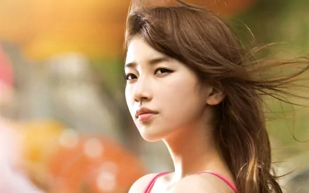 HD PC wallpaper featuring Bae Su Ji, also known as Bae Suzy, with her hair flowing against a colorful, blurred background, highlighting her serene expression.