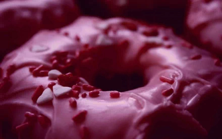 HD desktop wallpaper featuring a close-up of a pink-frosted doughnut with small red sprinkles, highlighting the rich texture and vibrant color.