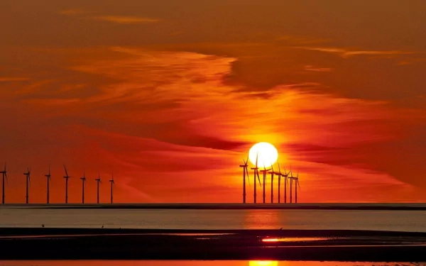 HD desktop wallpaper featuring a row of man-made windmills silhouetted against a vibrant orange sunset over calm water.