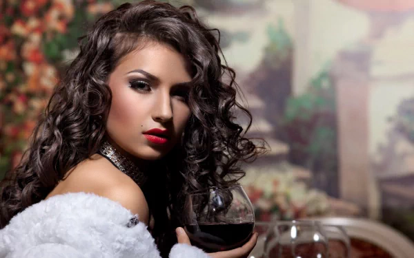 A beautiful woman with curly hair and bold red lips poses elegantly, holding a glass of wine, set against a floral backdrop. This 4K Ultra HD image serves as a striking desktop wallpaper.