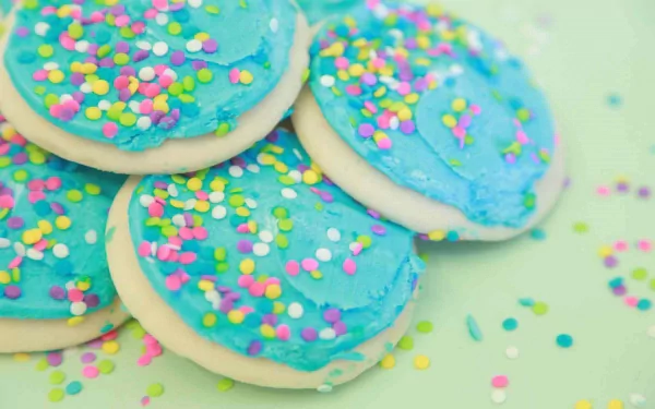 HD desktop wallpaper featuring close-up of round cookies with blue frosting and colorful sprinkles on a pastel background.