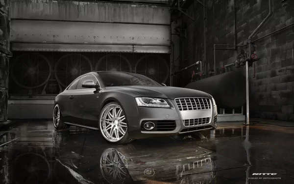 HD desktop wallpaper featuring a sleek Audi S5 parked in an industrial, dimly lit setting with reflective wet floor surfaces.