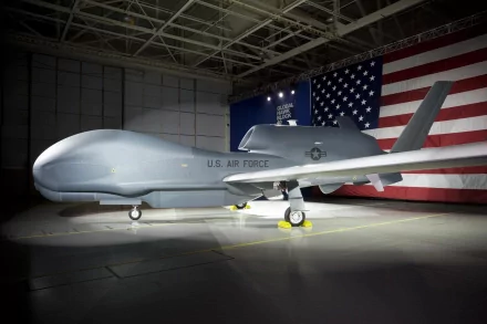 HD PC desktop wallpaper and background: military Northrop Grumman RQ-4 Global Hawk drone parked in a hangar, spotlighted against a large U.S. flag.