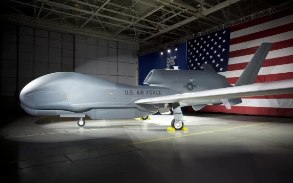 HD PC desktop wallpaper and background: military Northrop Grumman RQ-4 Global Hawk drone parked in a hangar, spotlighted against a large U.S. flag.