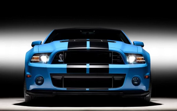 A striking HD desktop wallpaper featuring a Ford Mustang Shelby GT500, showcasing its sleek blue exterior and bold black stripes against a dramatic background.