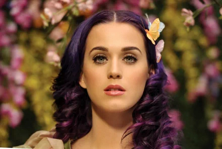 HD desktop wallpaper featuring Katy Perry with purple hair, adorned with a butterfly, against a background of colorful flowers.