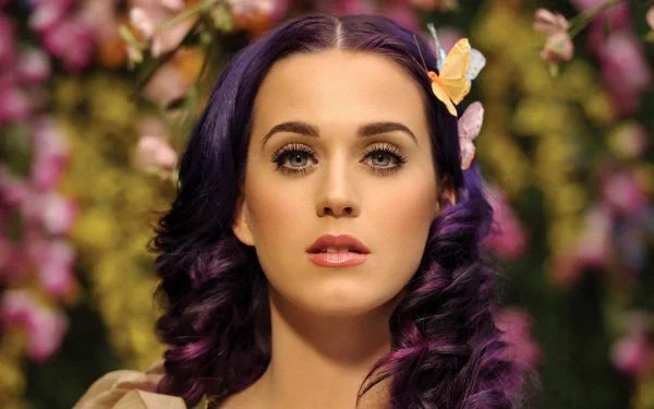HD desktop wallpaper featuring Katy Perry with purple hair, adorned with a butterfly, against a background of colorful flowers.