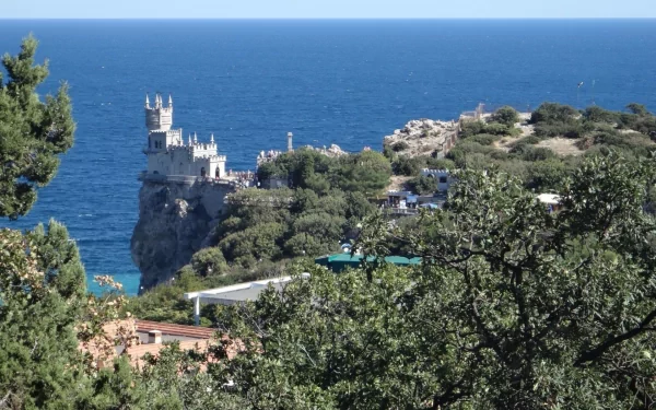 View of the Swallow's Nest castle perched on a cliff overlooking the Black Sea in Yalta, Russia, surrounded by lush greenery under a clear blue sky.