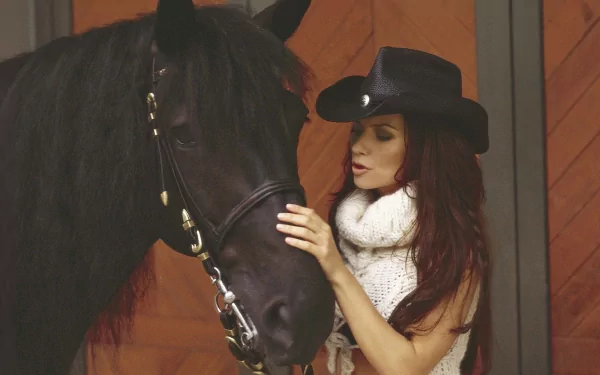 HD PC desktop wallpaper featuring Shania Twain in a black cowboy hat gently touching a dark horse inside a stable, capturing a serene country music moment.