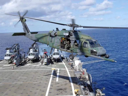 Military Sikorsky HH-60 Pave Hawk helicopter hovers above a ship deck with other helicopters, captured in HD quality as a desktop wallpaper and background image.