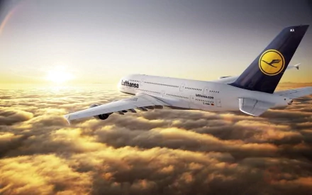 A stunning HD desktop wallpaper featuring an Airbus A380 soaring above fluffy clouds at sunset, showcasing its sleek design and Lufthansa branding against a golden sky.