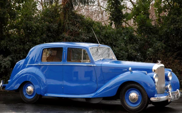 HD desktop wallpaper featuring a classic blue Bentley Mark VI vintage vehicle parked against a backdrop of dense greenery.