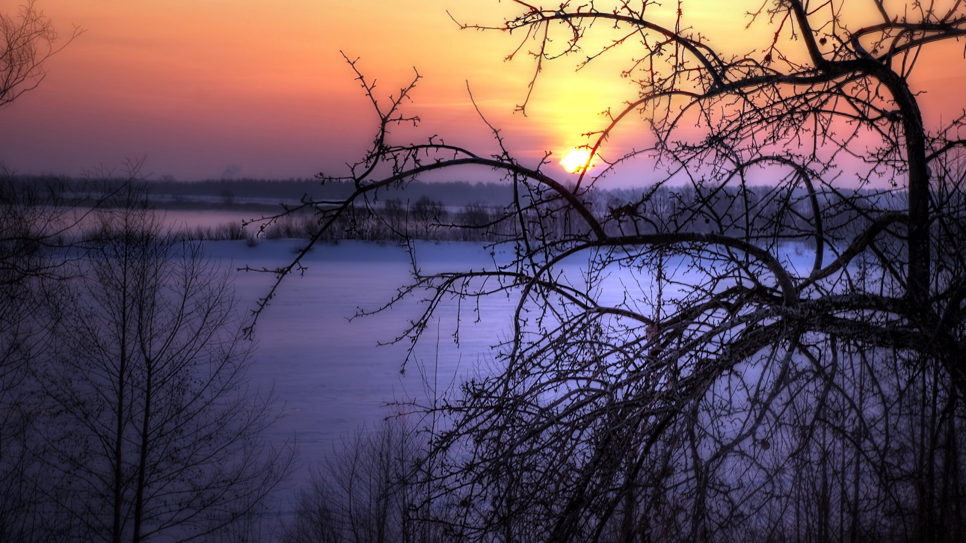 HD PC desktop wallpaper showcasing a serene nature scene with a vibrant sunset behind silhouetted branches over a calm, snowy landscape.