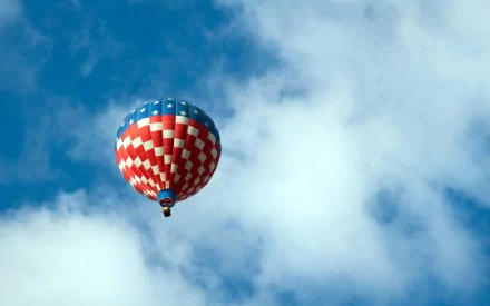 HD desktop wallpaper featuring a colorful red, white, and blue hot air balloon floating against a bright blue sky with white clouds.