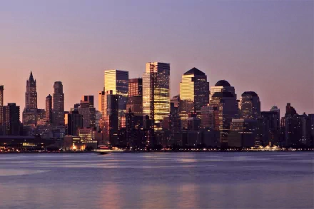 HD PC desktop wallpaper of New York skyline at dusk, man-made glass skyscrapers reflecting golden light across a calm river.