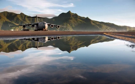 A Boeing C-17 Globemaster III parked on a runway, reflecting in a puddle with lush mountains in the background, showcasing military aviation in a stunning landscape.