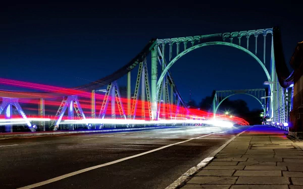Long-exposure photography time-lapse of a lit bridge at night with streaking red and blue vehicle light trails — 4K Ultra HD PC desktop wallpaper/background.