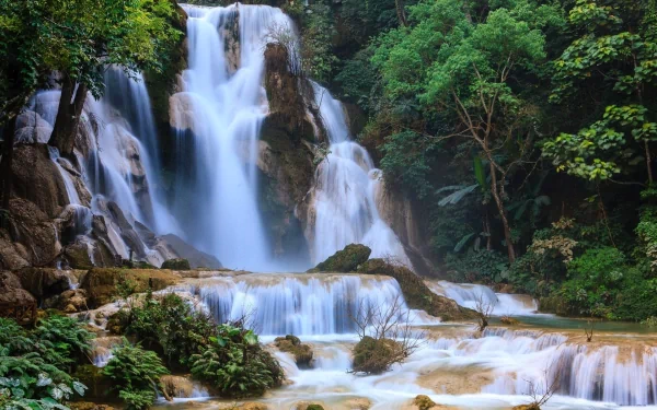 A vibrant HD desktop wallpaper featuring the lush tropical forest and cascading waters of Kuang Si Waterfall in Laos.