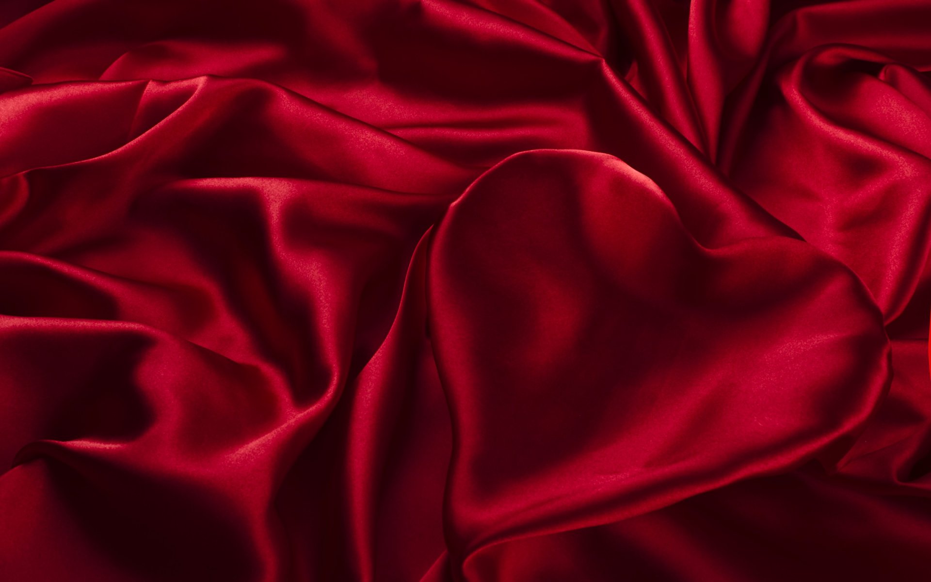 A rich, abstract red satin fabric drapes elegantly, featuring a heart shape subtly formed within the folds. This HD image serves as a striking desktop wallpaper or background.