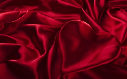 A rich, abstract red satin fabric drapes elegantly, featuring a heart shape subtly formed within the folds. This HD image serves as a striking desktop wallpaper or background.