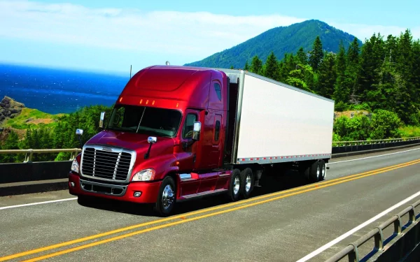 HD desktop wallpaper showcasing a red Freightliner truck driving on a scenic coastal highway with mountains and ocean in the background.