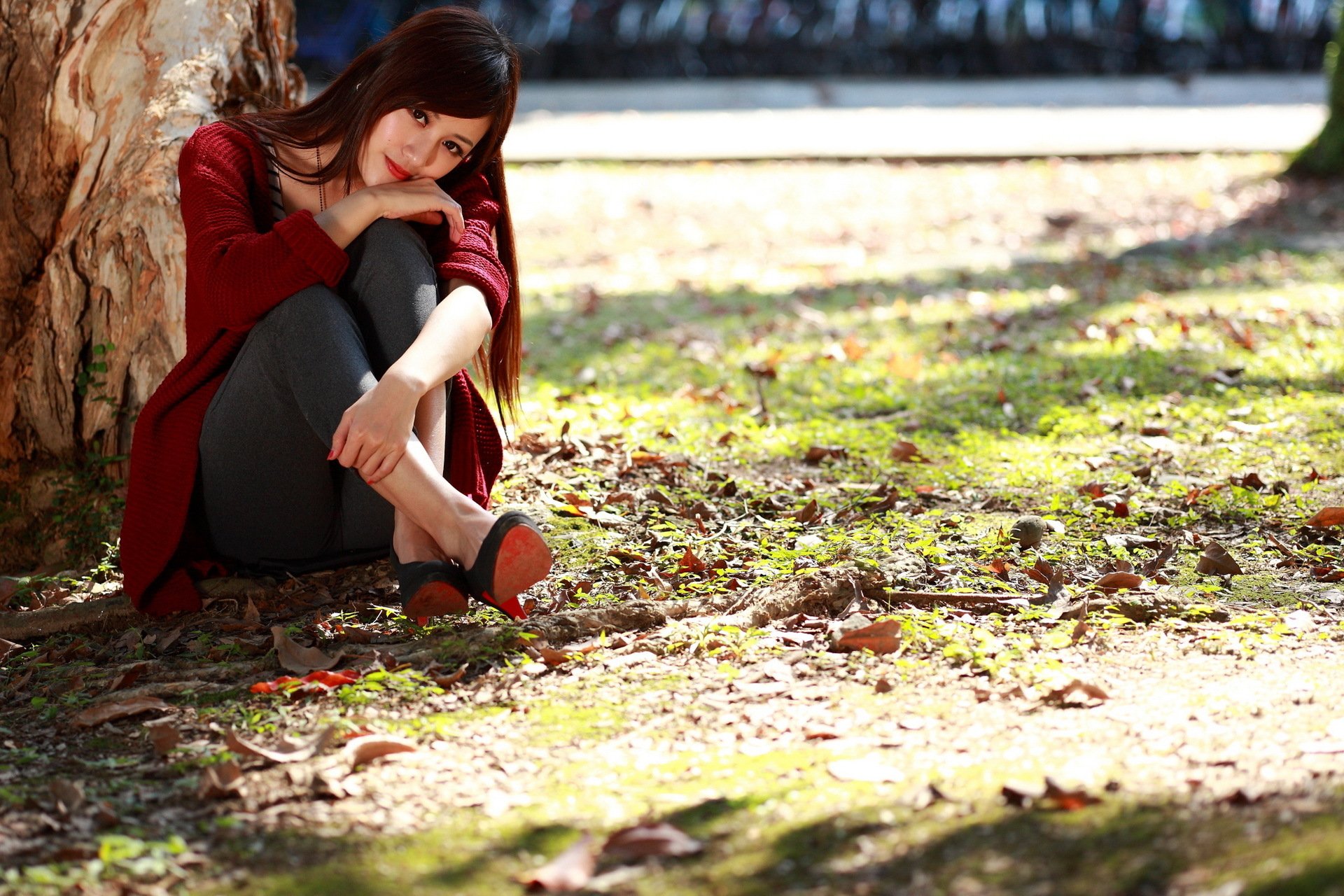 HD desktop wallpaper featuring an Asian woman sitting thoughtfully against a tree, surrounded by sunlit fallen leaves on the ground.