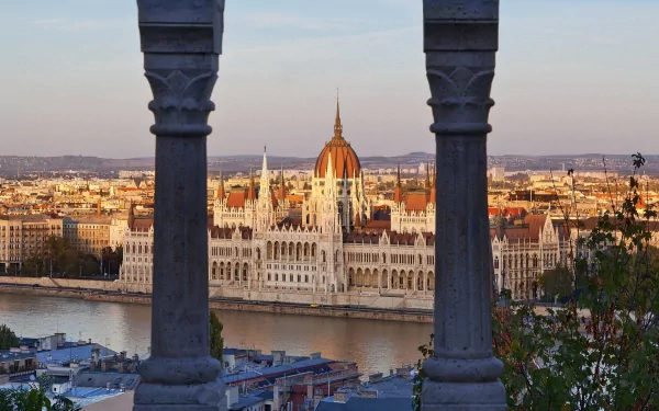 HD desktop wallpaper showcasing the Hungarian Parliament Building in Budapest, Hungary, framed between two architectural columns with the Danube River in the foreground.