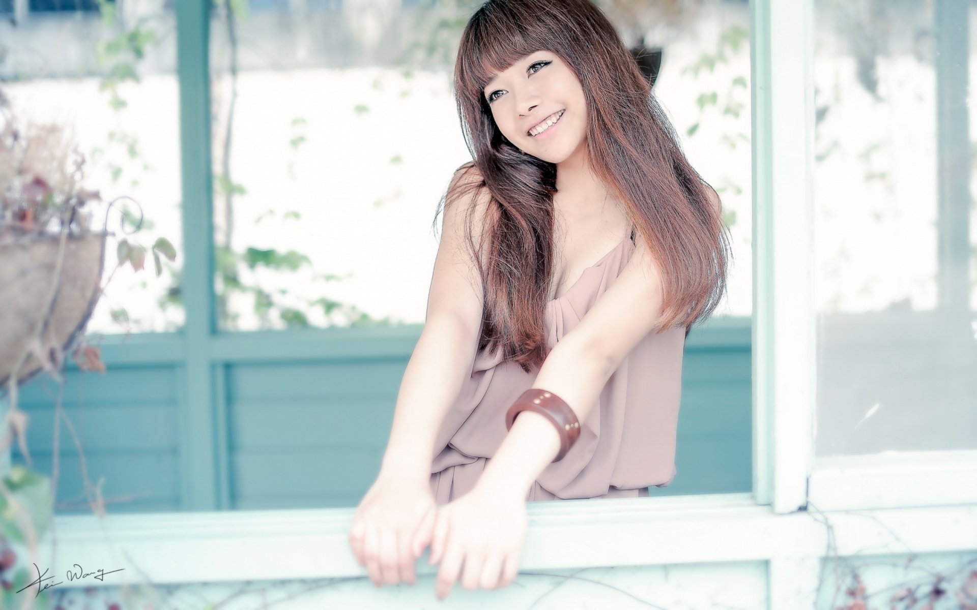 A smiling Asian woman with long hair leans playfully against a window frame, surrounded by soft, natural light, creating an inviting and serene atmosphere for an HD desktop wallpaper.