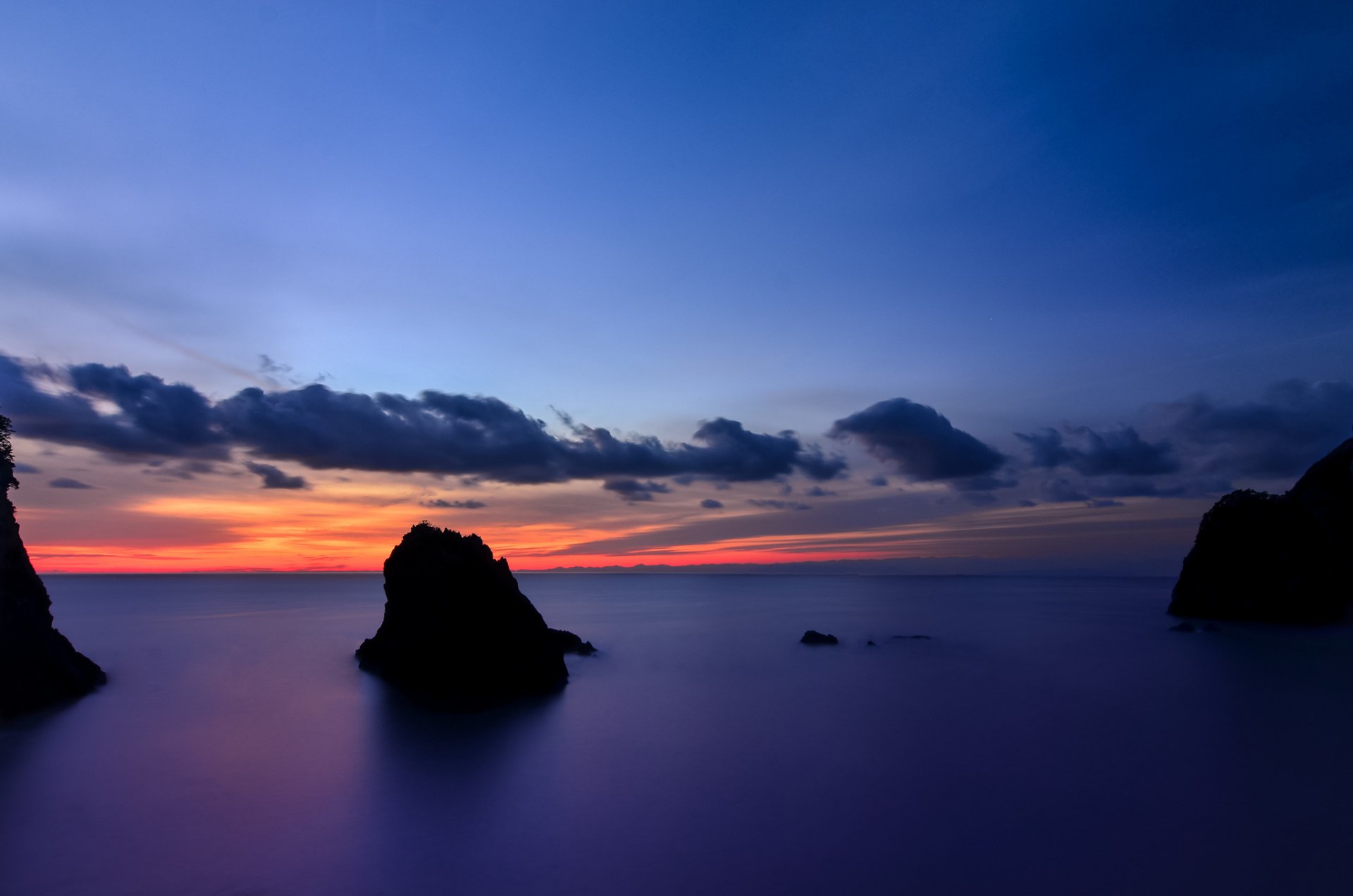 HD PC desktop wallpaper featuring a serene ocean scene at dusk with silhouetted rock formations and a colorful sky blending nature and tranquility.