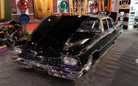 Black Cadillac LeBaron with chrome trim and open hood at an indoor car show, captured as a 2K Quad HD PC desktop wallpaper and background.