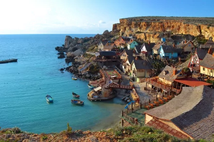 Scenic HD desktop wallpaper featuring the colorful man-made Popeye Village nestled along a rocky coastline with calm blue waters under a clear sky.