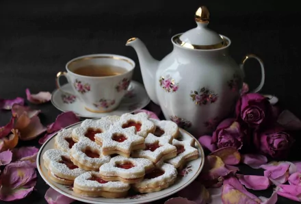HD PC desktop wallpaper featuring a plate of powdered sugar-dusted cookies with jam centers, a floral teapot, matching teacup, and scattered rose petals.