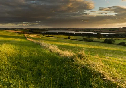 A serene English valley landscape featuring lush green fields and a calm river under a dramatic sky, showcasing the beauty of nature in Britain. HD desktop wallpaper.