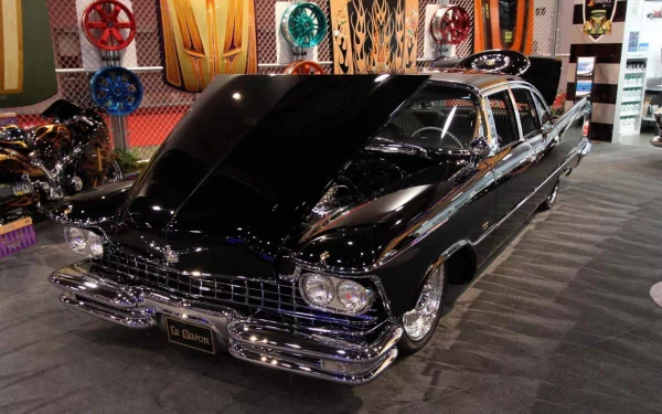 Black Cadillac LeBaron with chrome trim and open hood at an indoor car show, captured as a 2K Quad HD PC desktop wallpaper and background.