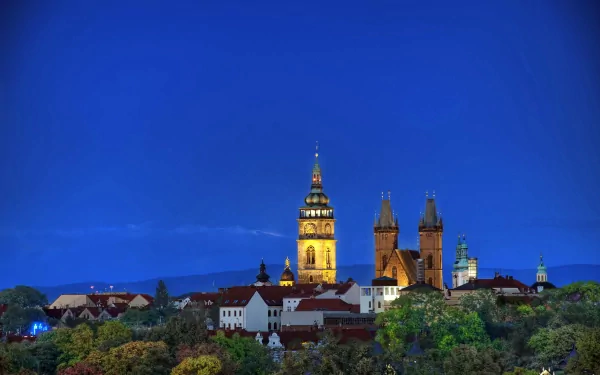 4K Ultra HD PC desktop wallpaper showing a man-made historic town skyline at dusk with illuminated church towers and rooftops beneath a deep blue sky.