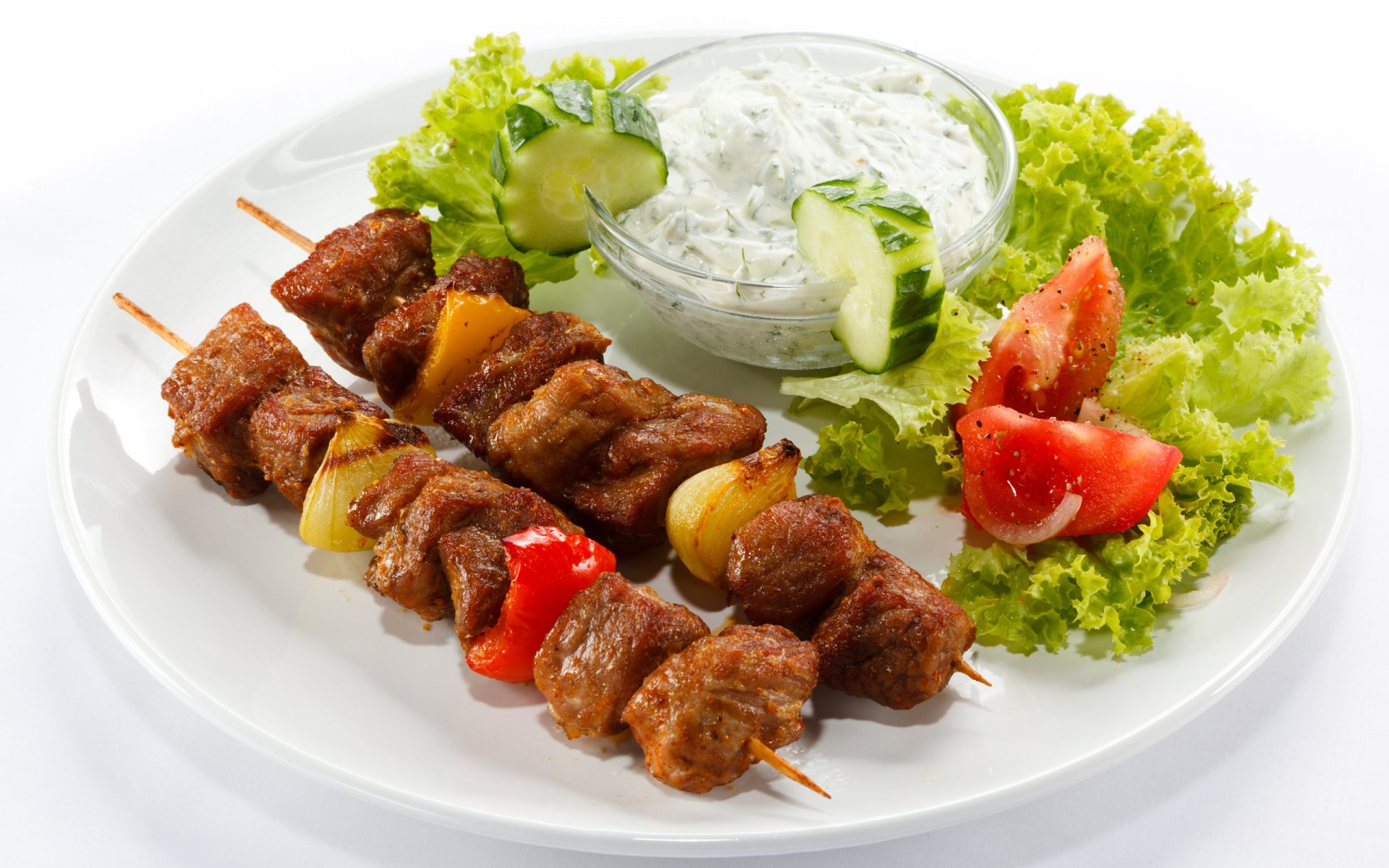 HD PC desktop wallpaper featuring succulent barbecue meat skewers with fresh lettuce, tomato, cucumber, and a bowl of creamy dip on a white plate.