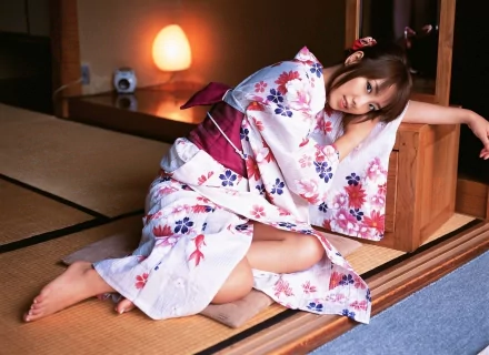 A woman in traditional Japanese clothes, featuring a floral pattern, sits on a tatami mat in a cozy room. This HD desktop wallpaper captures an elegant and serene moment.