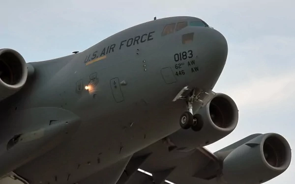Low-angle close-up of a military Boeing C-17 Globemaster III with landing gear down against a cloudy sky, HD PC desktop wallpaper/background.