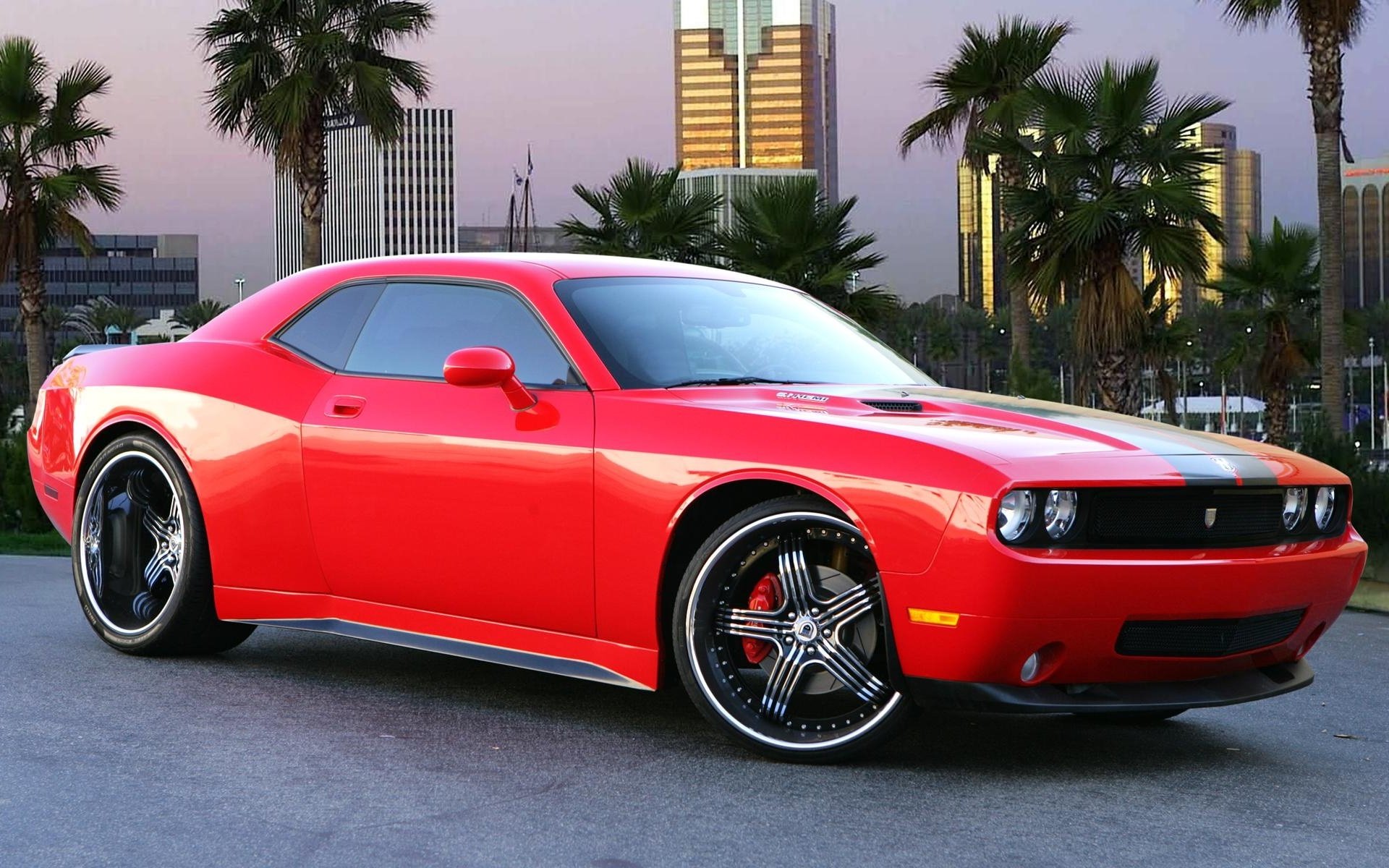 HD PC desktop wallpaper featuring a vibrant red Dodge Charger parked with palm trees and city skyscrapers in the background at dusk.