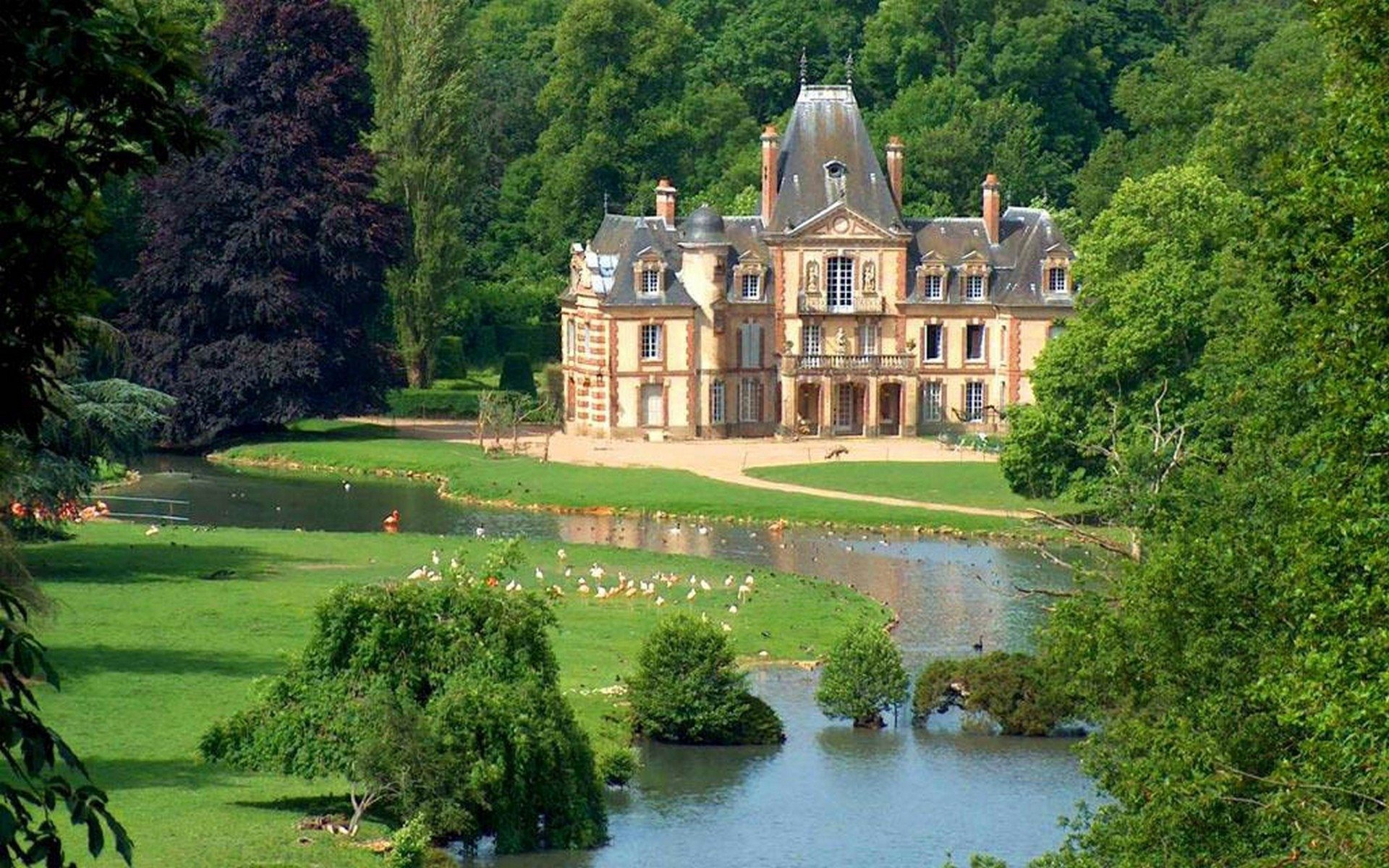 A stunning view of a man-made castle surrounded by lush greenery and a serene pond, creating an enchanting backdrop for a HD PC desktop wallpaper.