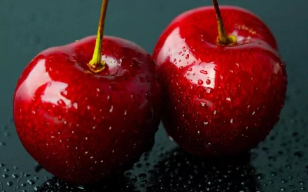 HD desktop wallpaper featuring two glossy red cherries with water droplets against a dark, reflective background.