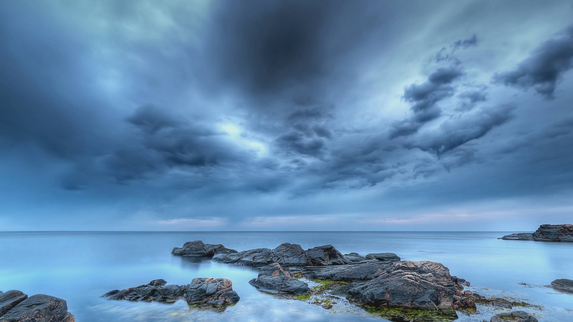 A serene ocean scene featuring rocky shores under a dramatic sky, capturing the tranquility of nature. An HD wallpaper that brings the beauty of the ocean to your desktop.