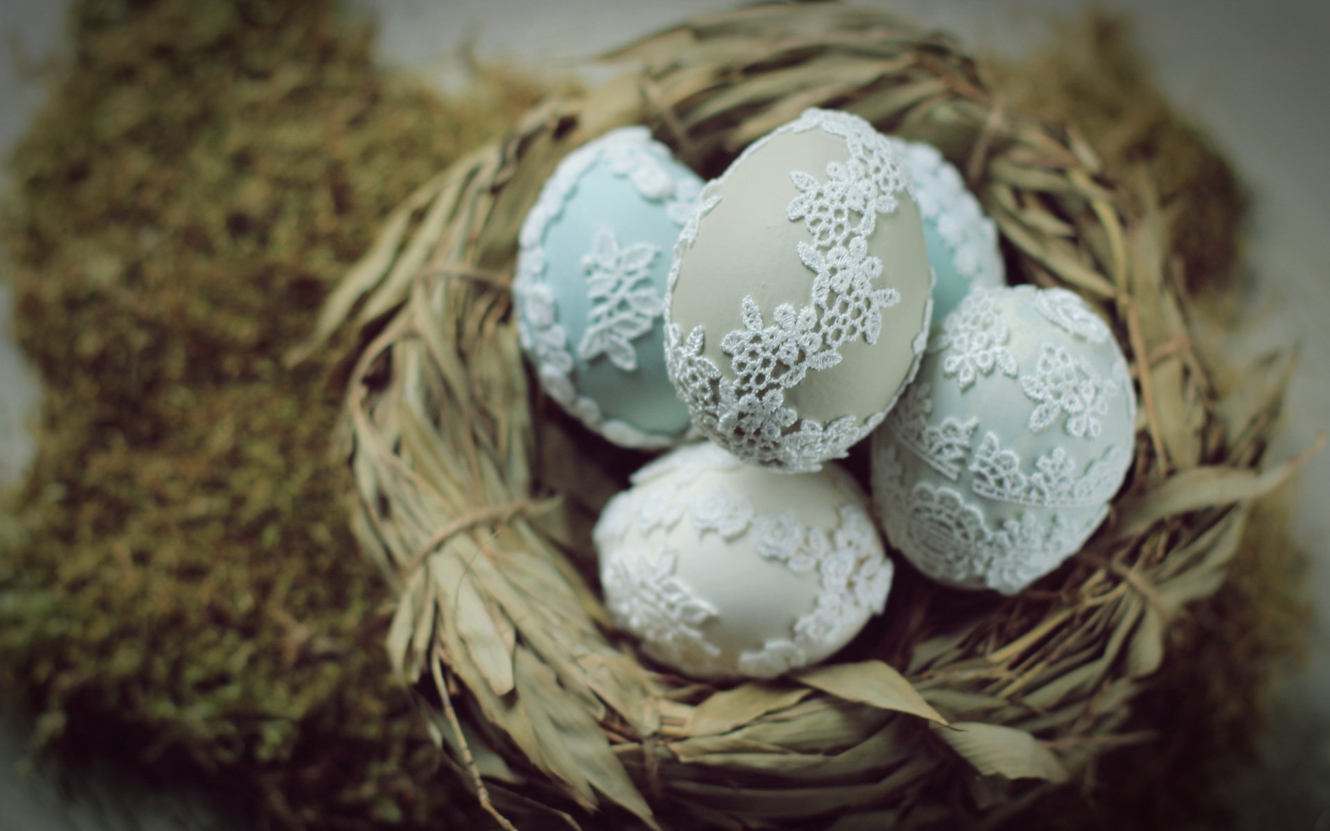 HD desktop wallpaper featuring intricately decorated Easter eggs with delicate white lace patterns nestled in a rustic straw nest, evoking a serene holiday atmosphere.