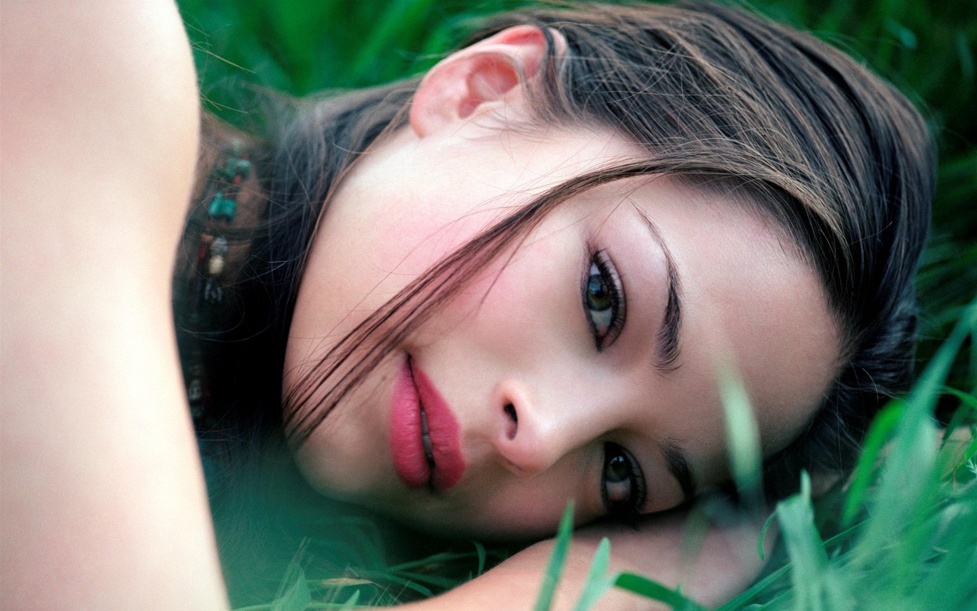 A close-up of Kristin Kreuk lying on green grass, gazing softly with her hair cascading around her face. This HD image serves as a striking desktop wallpaper.