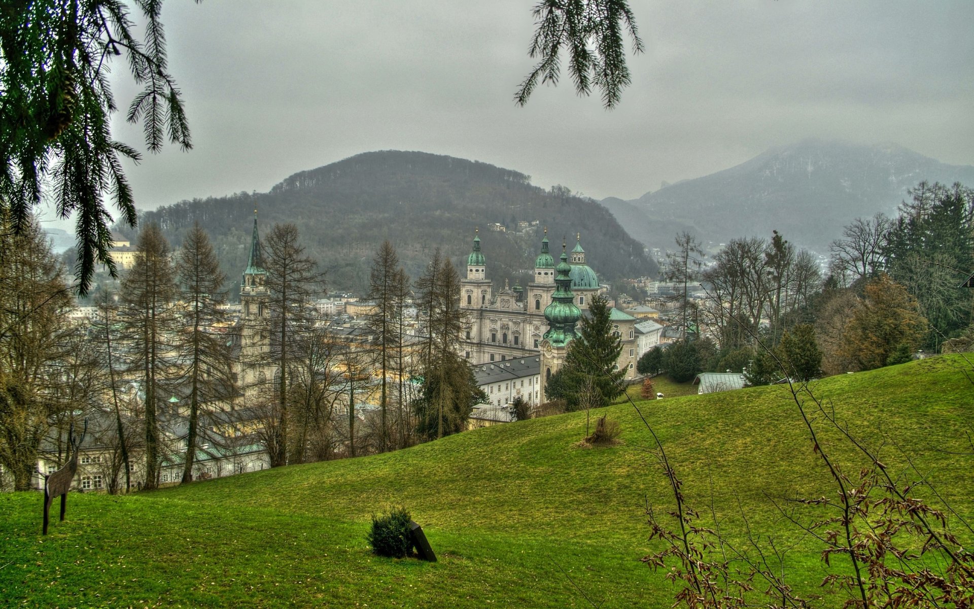 Scenic view of Salzburg, Austria, showcasing a historic town nestled among hills and greenery under an overcast sky, captured in a high-definition desktop wallpaper.