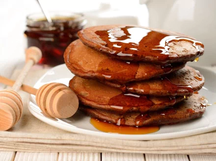 HD desktop wallpaper featuring a stack of golden pancakes drizzled with syrup, accompanied by honey dippers and a jar of honey in the background.