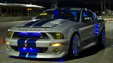 A high-definition desktop wallpaper featuring a Ford Mustang Shelby GT500 with blue accents illuminated, parked under nighttime lighting.