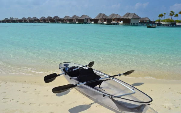 4K Ultra HD PC desktop wallpaper: a small kayak boat vehicle rests on white sand beside clear turquoise water, with overwater bungalows along the distant horizon.