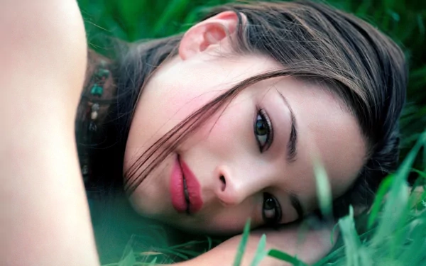 A close-up of Kristin Kreuk lying on green grass, gazing softly with her hair cascading around her face. This HD image serves as a striking desktop wallpaper.