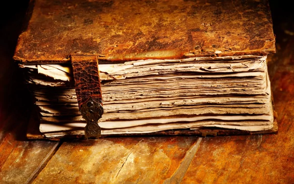 A close-up of an aged, leather-bound book with frayed pages and a metal clasp, set on a rustic wooden surface. This 4K Ultra HD image serves as a captivating desktop wallpaper.